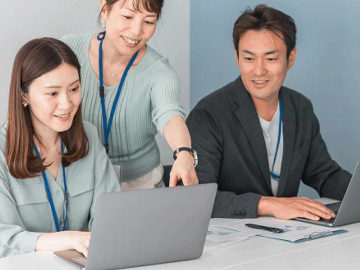 オフィスでパソコンを見ながら3人が話している写真